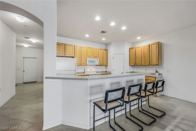 kitchen featuring light brown cabinetry, white appliances, kitchen peninsula, and a kitchen bar