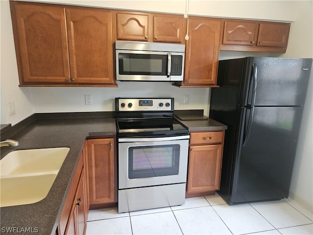 kitchen with sink, black fridge, light tile patterned floors, and range with electric stovetop