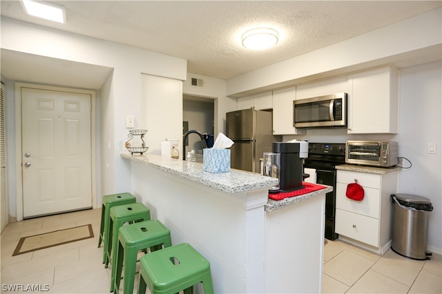 kitchen with white cabinetry, light tile patterned floors, kitchen peninsula, appliances with stainless steel finishes, and a kitchen bar