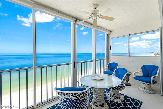 sunroom with a water view, ceiling fan, and a beach view