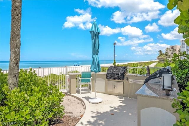 view of patio featuring exterior kitchen, a water view, area for grilling, and a view of the beach