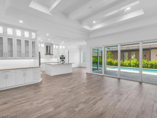 unfurnished living room with sink, beam ceiling, light hardwood / wood-style flooring, and a towering ceiling