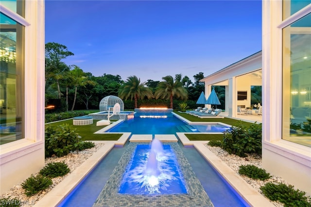 pool at dusk with an in ground hot tub, pool water feature, and a patio area