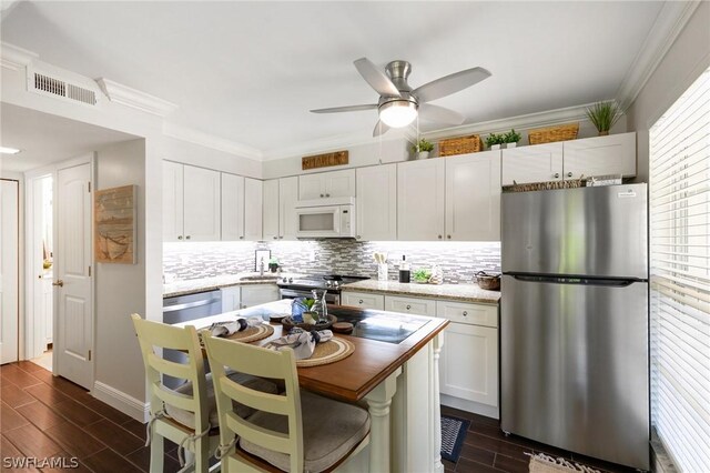 kitchen with white cabinets, ceiling fan, stainless steel appliances, light stone countertops, and decorative backsplash