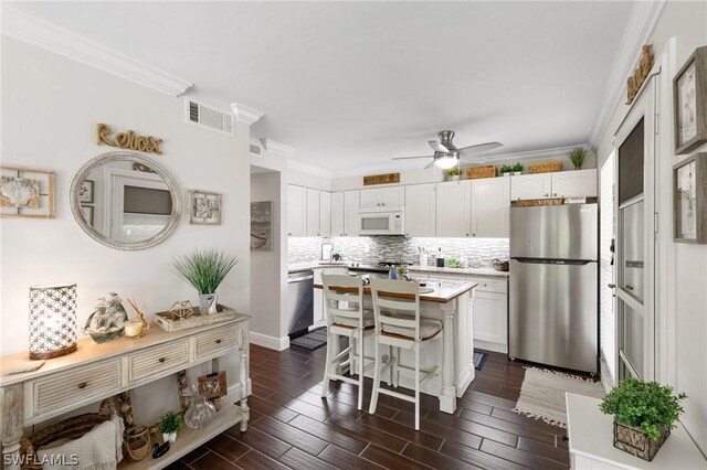 kitchen with appliances with stainless steel finishes, white cabinets, backsplash, a center island, and ceiling fan