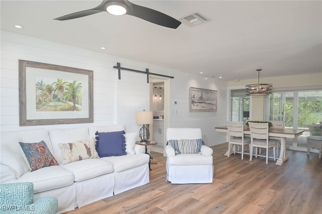 living room featuring hardwood / wood-style floors, ceiling fan with notable chandelier, and a barn door