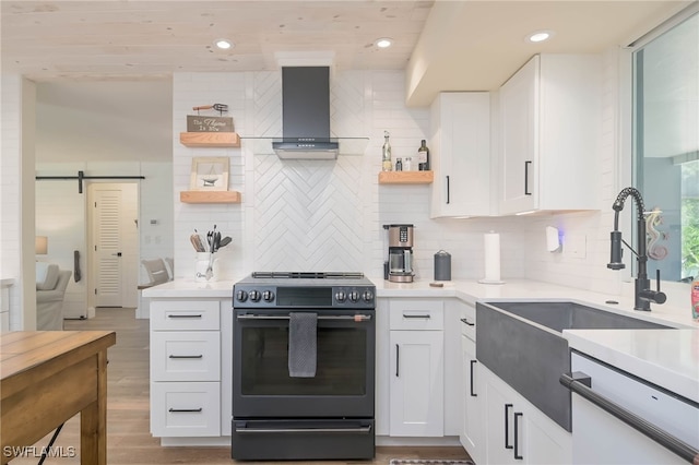 kitchen featuring backsplash, wall chimney exhaust hood, electric stove, a barn door, and white cabinets