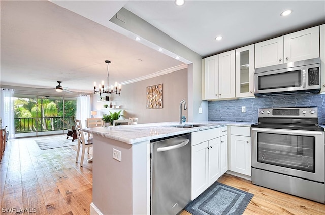 kitchen featuring ceiling fan with notable chandelier, light stone countertops, appliances with stainless steel finishes, light hardwood / wood-style flooring, and kitchen peninsula