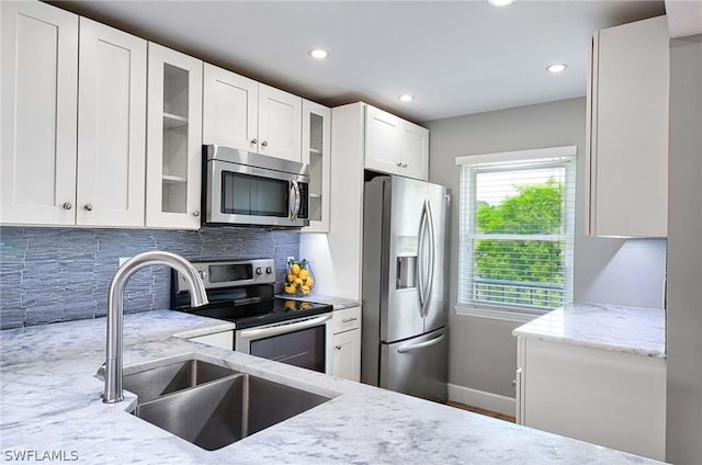 kitchen featuring tasteful backsplash, sink, white cabinetry, stainless steel appliances, and light stone counters