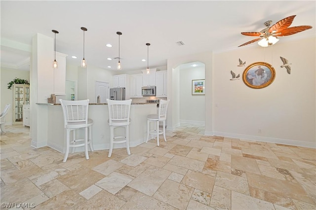 kitchen with appliances with stainless steel finishes, decorative light fixtures, a kitchen breakfast bar, and white cabinets