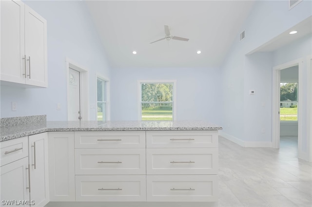 kitchen featuring light stone counters, white cabinets, ceiling fan, and a healthy amount of sunlight