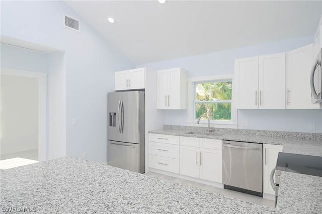 kitchen with lofted ceiling, sink, stainless steel appliances, white cabinets, and light stone counters