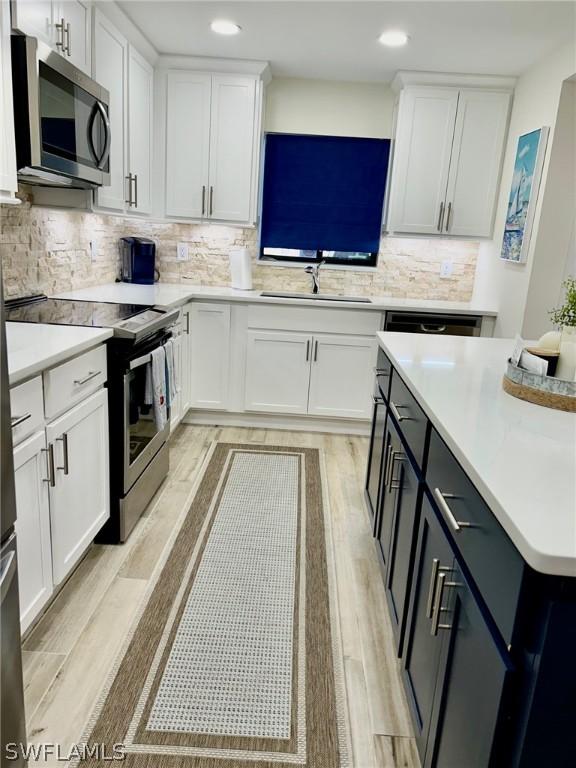 kitchen featuring appliances with stainless steel finishes, sink, white cabinets, decorative backsplash, and light hardwood / wood-style flooring