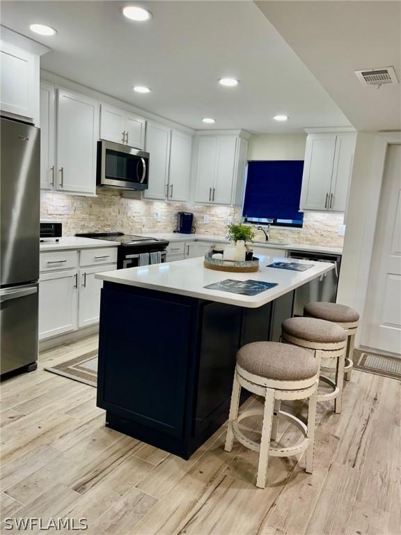 kitchen with a kitchen island, white cabinetry, appliances with stainless steel finishes, and light hardwood / wood-style floors