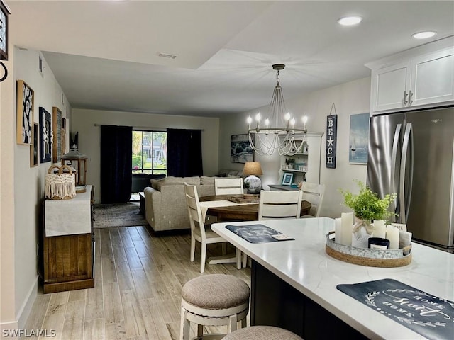 kitchen with decorative light fixtures, a chandelier, light hardwood / wood-style flooring, stainless steel refrigerator, and white cabinets