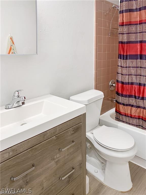 full bathroom with shower / bath combo with shower curtain, wood-type flooring, toilet, and vanity