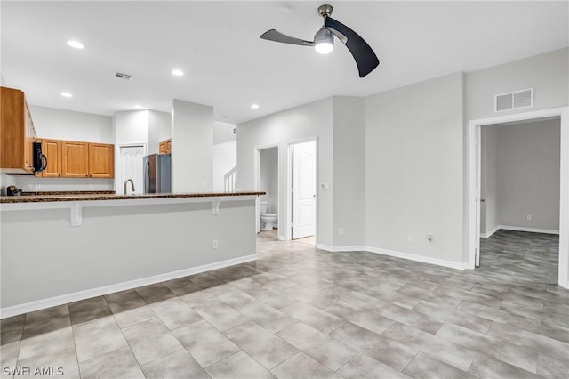 kitchen featuring a breakfast bar, sink, dark stone countertops, stainless steel fridge, and ceiling fan