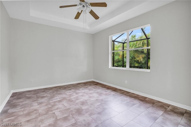 spare room with a raised ceiling, light tile patterned floors, and ceiling fan