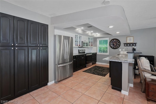 kitchen with light tile patterned flooring, appliances with stainless steel finishes, a kitchen breakfast bar, light stone counters, and kitchen peninsula