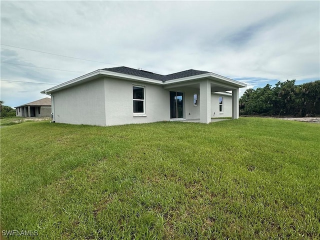 back of property featuring stucco siding, a shingled roof, and a yard