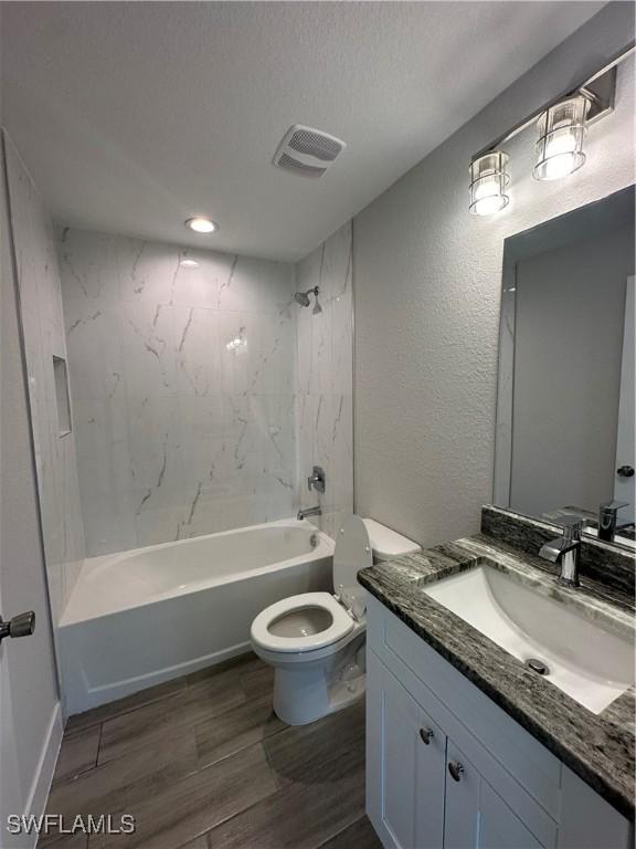 bathroom featuring shower / bath combination, visible vents, a textured wall, toilet, and vanity