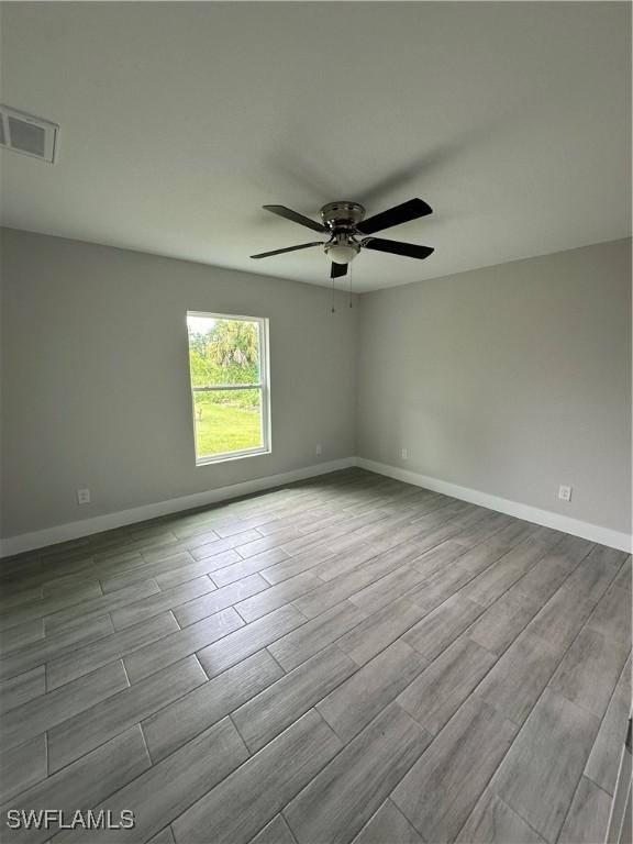 spare room with ceiling fan, visible vents, baseboards, and wood finished floors