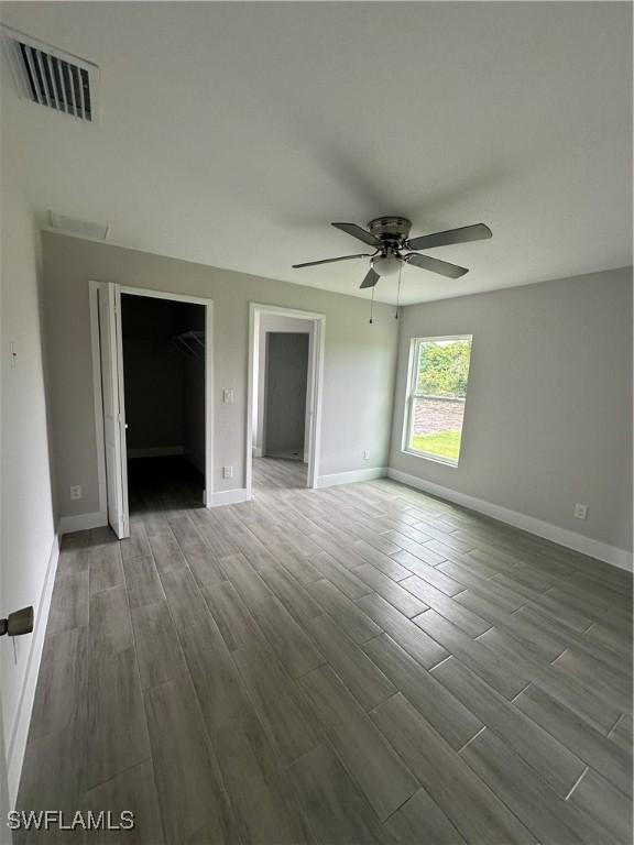 unfurnished bedroom with wood finish floors, visible vents, a spacious closet, and baseboards