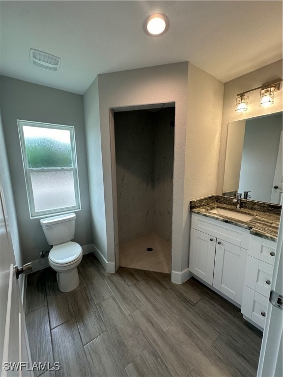 bathroom featuring toilet, a tile shower, and vanity