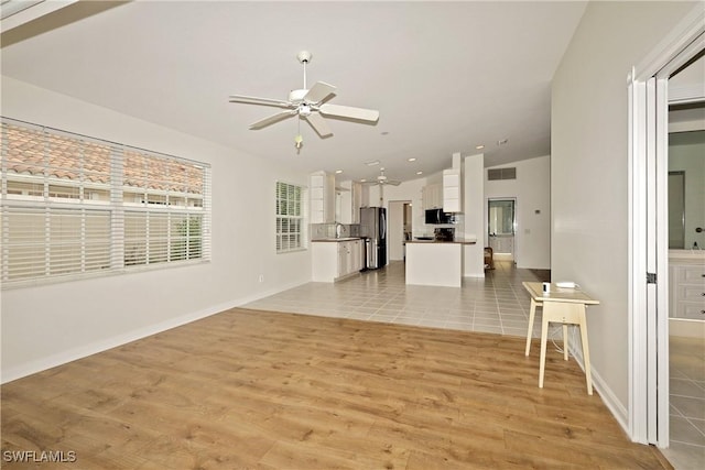 unfurnished living room with lofted ceiling, light wood finished floors, baseboards, and a ceiling fan