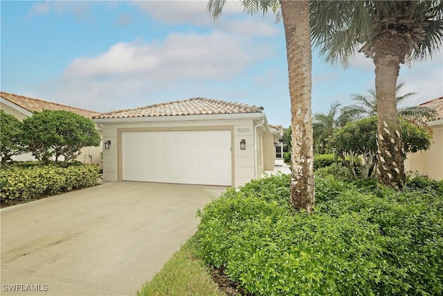 view of front of property featuring a garage, a tile roof, concrete driveway, and stucco siding