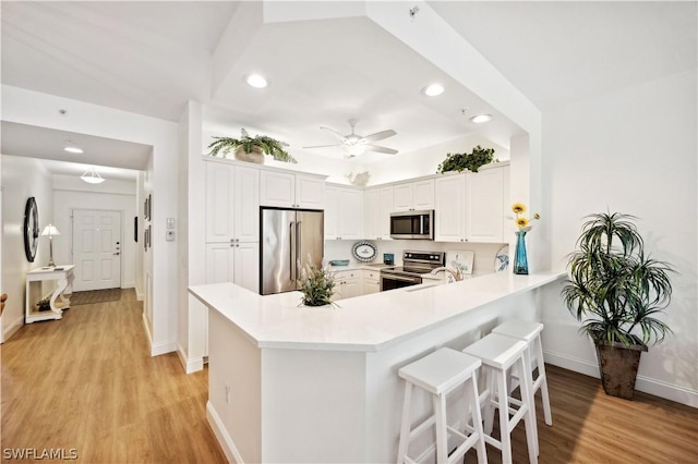 kitchen with white cabinetry, appliances with stainless steel finishes, kitchen peninsula, ceiling fan, and light hardwood / wood-style floors