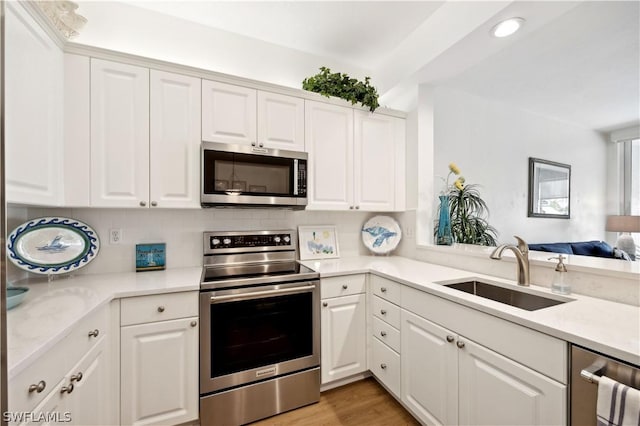 kitchen with sink, white cabinetry, light wood-type flooring, stainless steel appliances, and backsplash