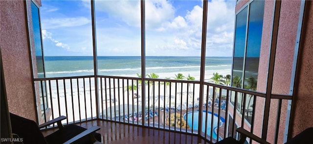 unfurnished sunroom with plenty of natural light, a water view, and a beach view