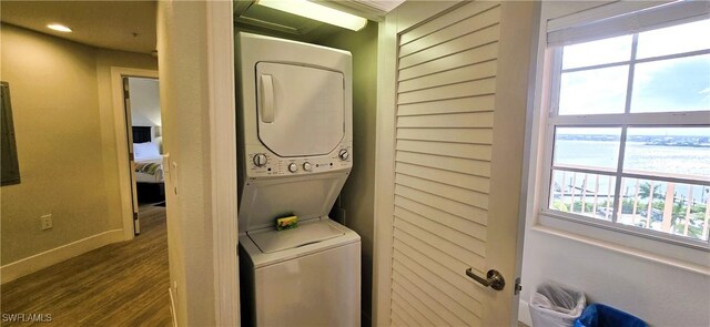 clothes washing area featuring stacked washer / drying machine, a healthy amount of sunlight, and wood-type flooring