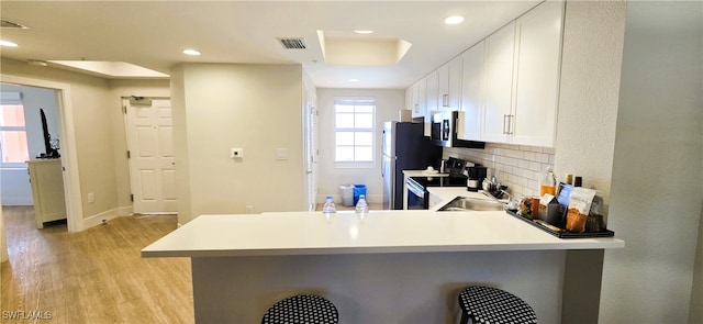 kitchen featuring kitchen peninsula, decorative backsplash, appliances with stainless steel finishes, white cabinetry, and a breakfast bar area