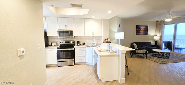 kitchen featuring ceiling fan, tasteful backsplash, kitchen peninsula, white cabinets, and appliances with stainless steel finishes