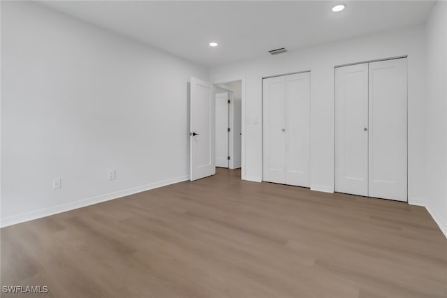 unfurnished bedroom with multiple closets and hardwood / wood-style flooring