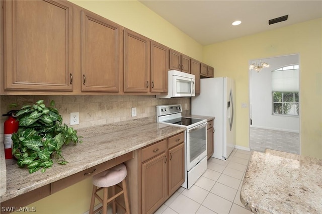 kitchen with light tile patterned floors, white appliances, backsplash, light stone counters, and a kitchen bar