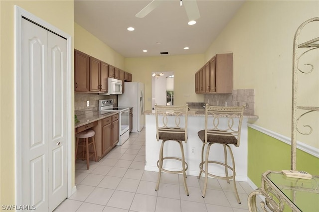 kitchen with a kitchen breakfast bar, decorative backsplash, light tile patterned floors, kitchen peninsula, and white appliances