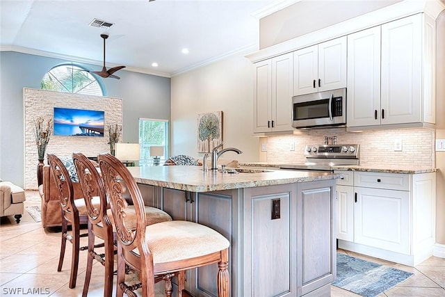 kitchen with an island with sink, appliances with stainless steel finishes, white cabinets, and a kitchen bar