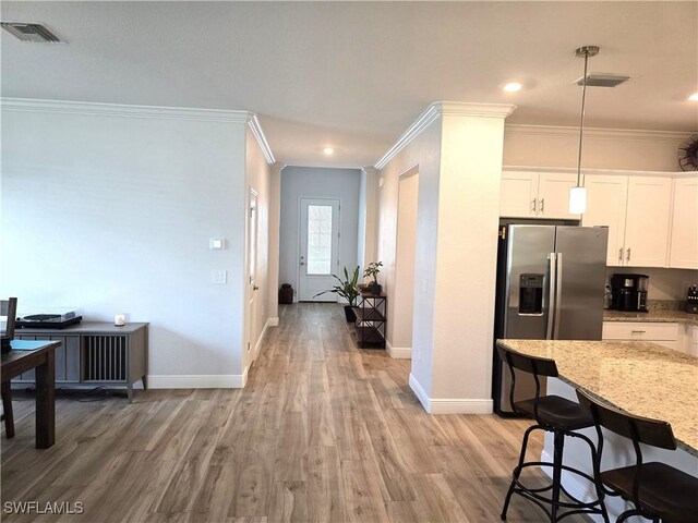 kitchen with wood-type flooring, pendant lighting, stainless steel fridge, white cabinets, and light stone countertops