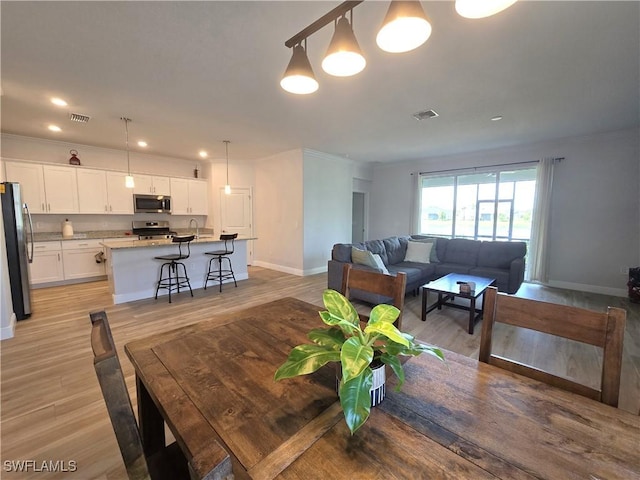 dining room with ornamental molding and light hardwood / wood-style flooring