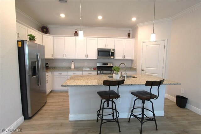 kitchen with stainless steel appliances, a kitchen island with sink, decorative light fixtures, and light wood-type flooring