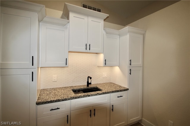 kitchen featuring sink, dark stone counters, tasteful backsplash, and white cabinetry