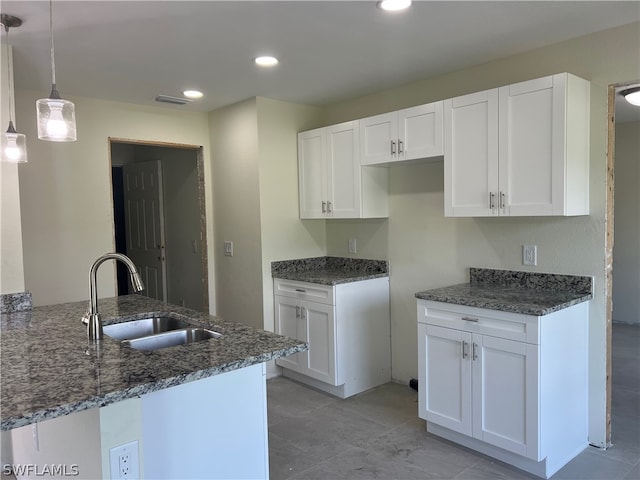 kitchen featuring dark stone counters, decorative light fixtures, kitchen peninsula, sink, and white cabinets