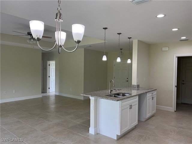 kitchen with pendant lighting, ceiling fan with notable chandelier, light stone counters, sink, and white cabinets