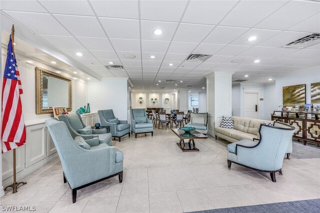 tiled living room with decorative columns and a drop ceiling