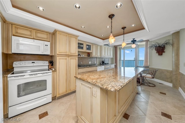 kitchen featuring light stone counters, a tray ceiling, crown molding, a kitchen island, and white appliances