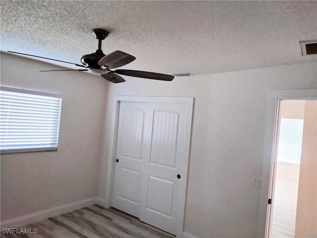 unfurnished bedroom with a textured ceiling, ceiling fan, light hardwood / wood-style flooring, and a closet