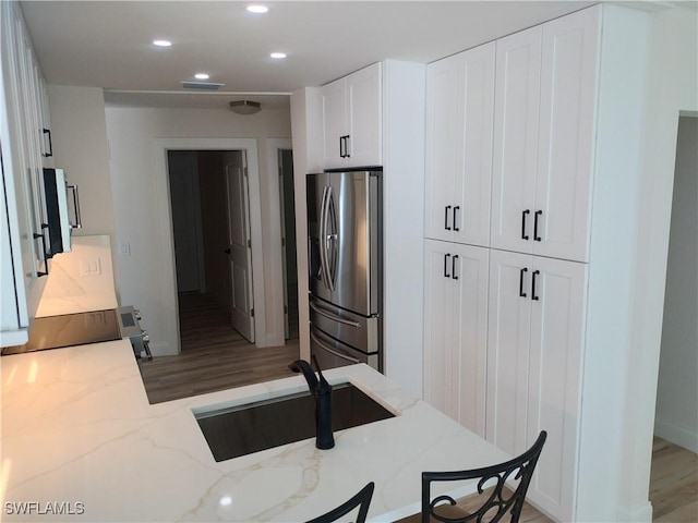 kitchen featuring white cabinetry, sink, light stone counters, stainless steel refrigerator with ice dispenser, and light wood-type flooring